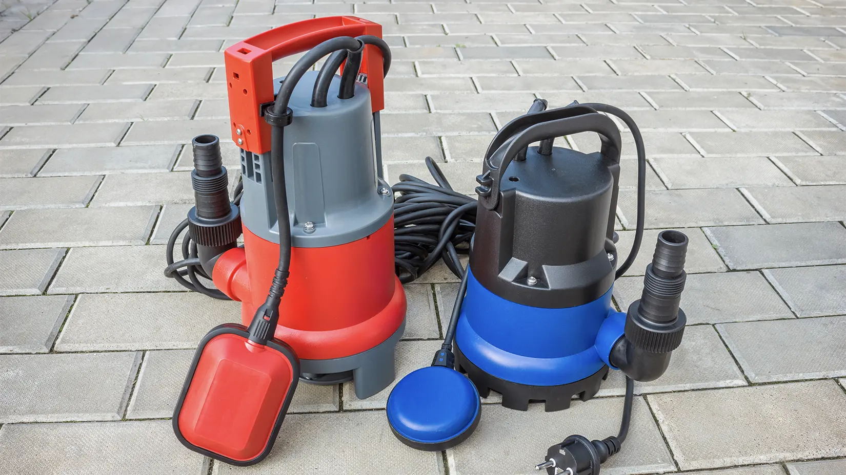 A red and blue sump pump sit next to each other on a concrete pavement.
